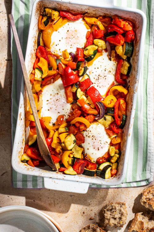 Four baked eggs in a rectangular baking dish with summer vegetables.