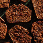 Several slices of pumpkin quick bread in hard light on green marble.