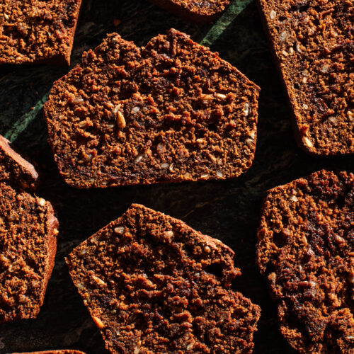 Several slices of pumpkin quick bread in hard light on green marble.