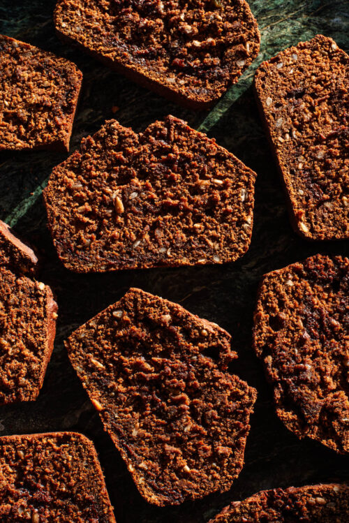 Several slices of pumpkin quick bread in hard light on green marble.