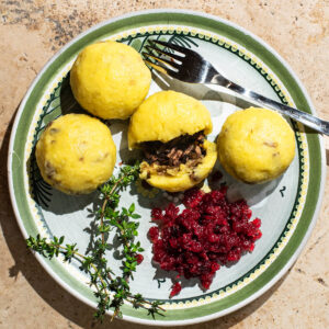 A plate with four filled dumplings, one split to show filling, and lingonberry sauce.