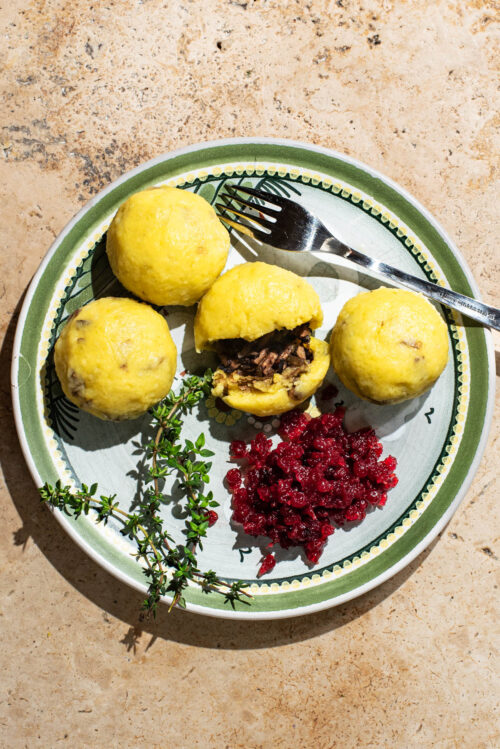A plate with four filled dumplings, one split to show filling, and lingonberry sauce.