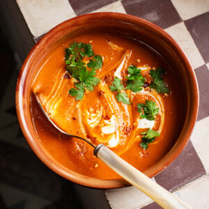 Thick orange soup on a checkered window ledge, topped with cream and parsley.
