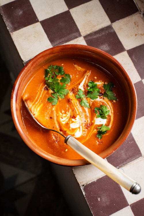 Thick orange soup on a checkered window ledge, topped with cream and parsley.
