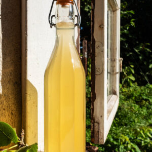 A glass flip-top bottle filled with a light yellow vinegar on a windowsill.