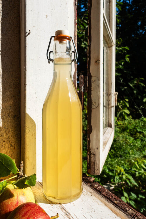 A glass flip-top bottle filled with a light yellow vinegar on a windowsill.