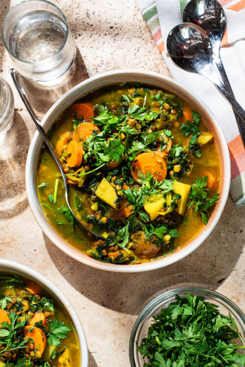 A bowl of carrot and potato soup topped with fresh parsley.