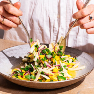 Woman's hands tossing a mango vegetable salad in a serving bowl.