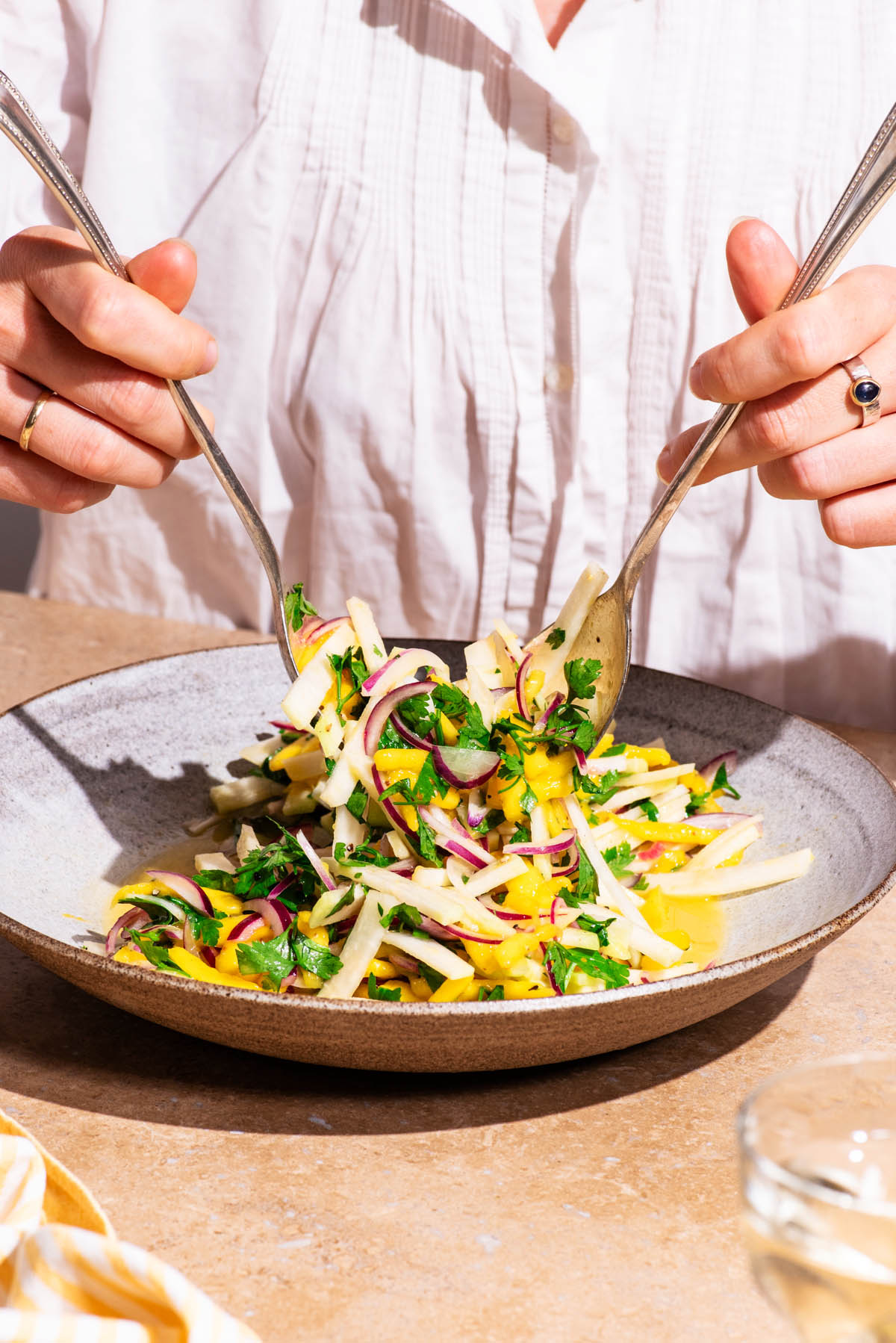 Woman's hands tossing a mango vegetable salad in a serving bowl.