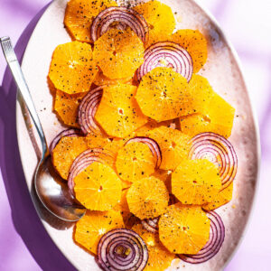 A platter of thinly sliced oranges and red onions with black pepper.