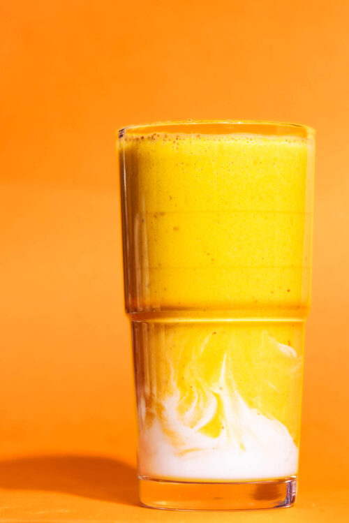 A lighter orange smoothie in a glass with yoghurt swirled at the base, against a darker orange background.