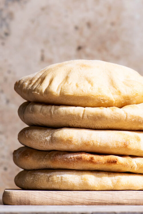 A stack of pitas on a small wooden cutting board.