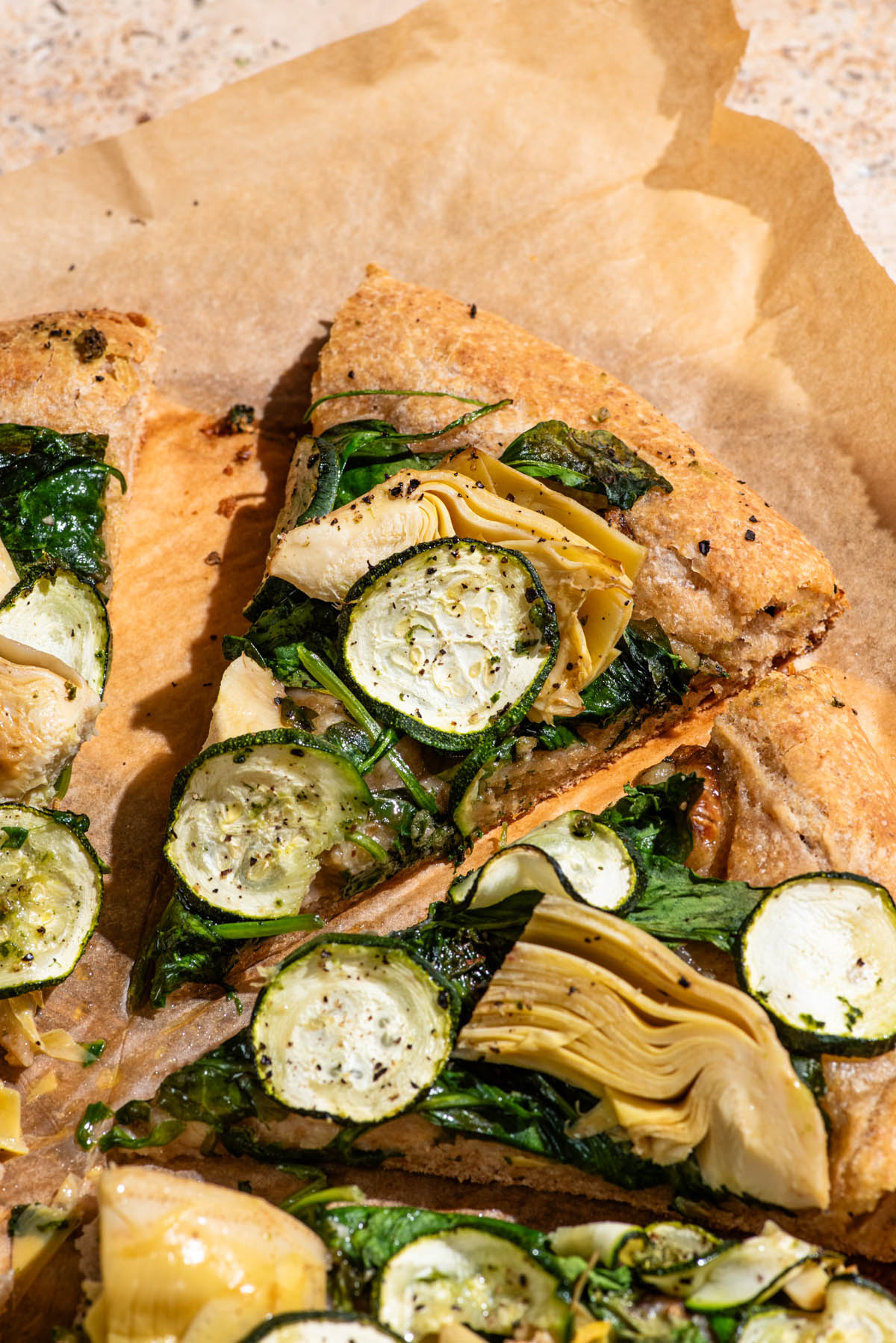 Slices of vegetable pizza with greens, artichoke hearts, and zucchini rounds.