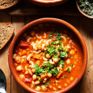 Two bowls of tomato soup with pasta and chickpeas, topped with chopped parsley.