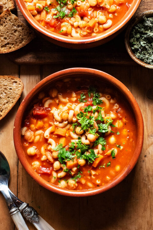 Two bowls of tomato soup with pasta and chickpeas, topped with chopped parsley.