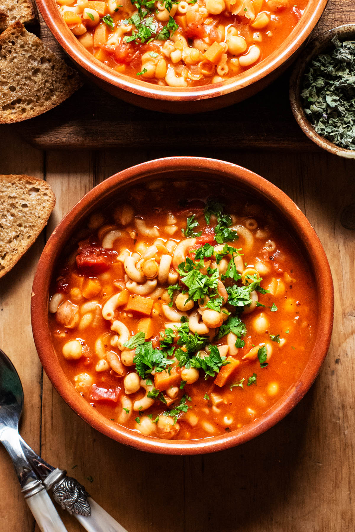 Two bowls of tomato soup with pasta and chickpeas, topped with chopped parsley.