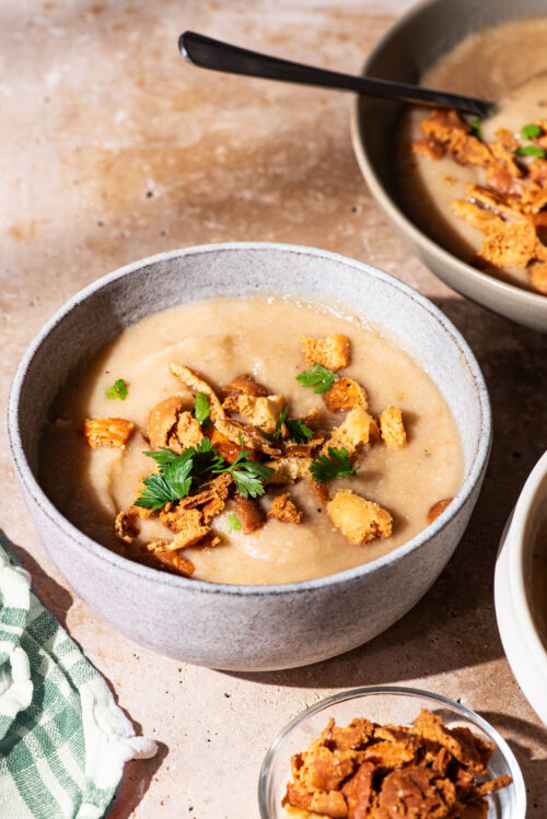 Bowls of pale creamy soup topped with flatbread crackers and parsley.