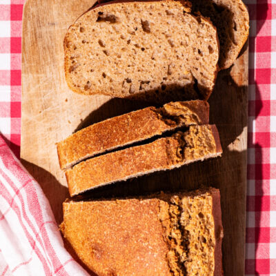 A loaf of bread with four slices cut, two laying down to show interior texture.