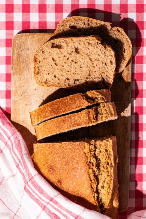 A loaf of bread with four slices cut, two laying down to show interior texture.