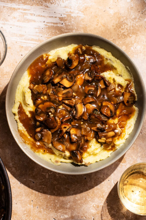 A bowl full of mashed potatoes topped with mushroom gravy.