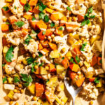 Vegetable tray bake with tahini sauce and parsley on the baking sheet with a serving spoon.