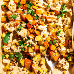 Vegetable tray bake with tahini sauce and parsley on the baking sheet with a serving spoon.