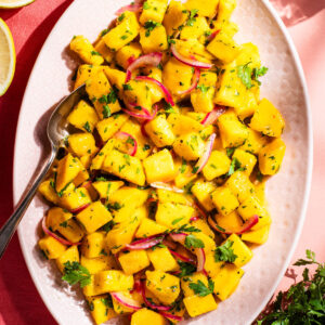 Pieces of mango on a serving platter with a dressing, herbs, and red onion.