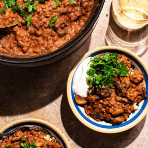 Vegetable curry in two small bowls with yogurt and parsley, pot of curry in the corner.