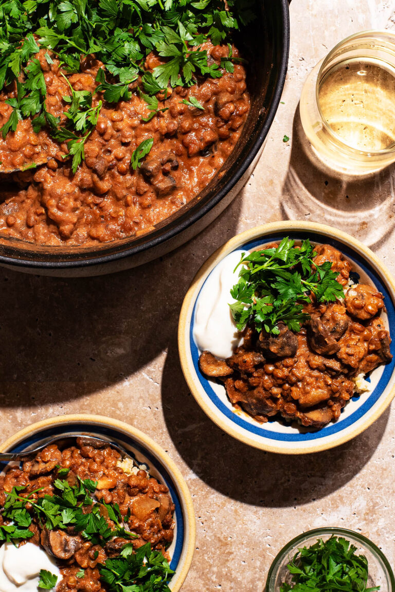 Vegetable curry in two small bowls with yogurt and parsley, pot of curry in the corner.