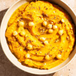 Light orange dip in a shallow bowl topped with oil, spices, and chickpeas.
