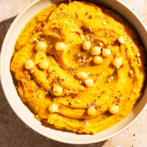 Light orange dip in a shallow bowl topped with oil, spices, and chickpeas.