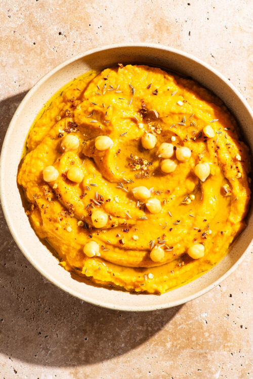 Light orange dip in a shallow bowl topped with oil, spices, and chickpeas.