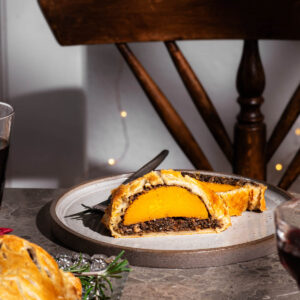A squash wellington slice on a plate with a wooden chair and lights behind.