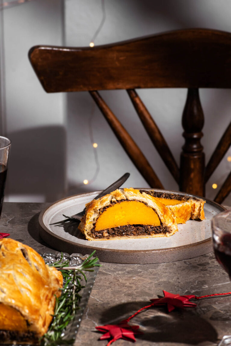 A squash wellington slice on a plate with a wooden chair and lights behind.
