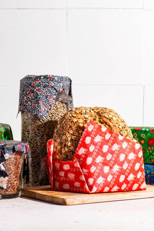 Several jars, containers, and half a loaf of bread wrapped in colourful wax wraps.