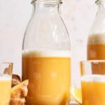 A ginger drink in clear glass bottles and small glasses with lemon and ginger around.