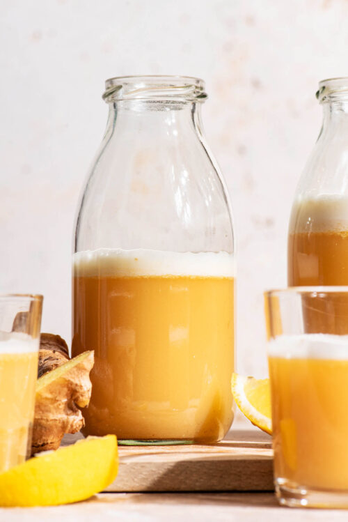 A ginger drink in clear glass bottles and small glasses with lemon and ginger around.