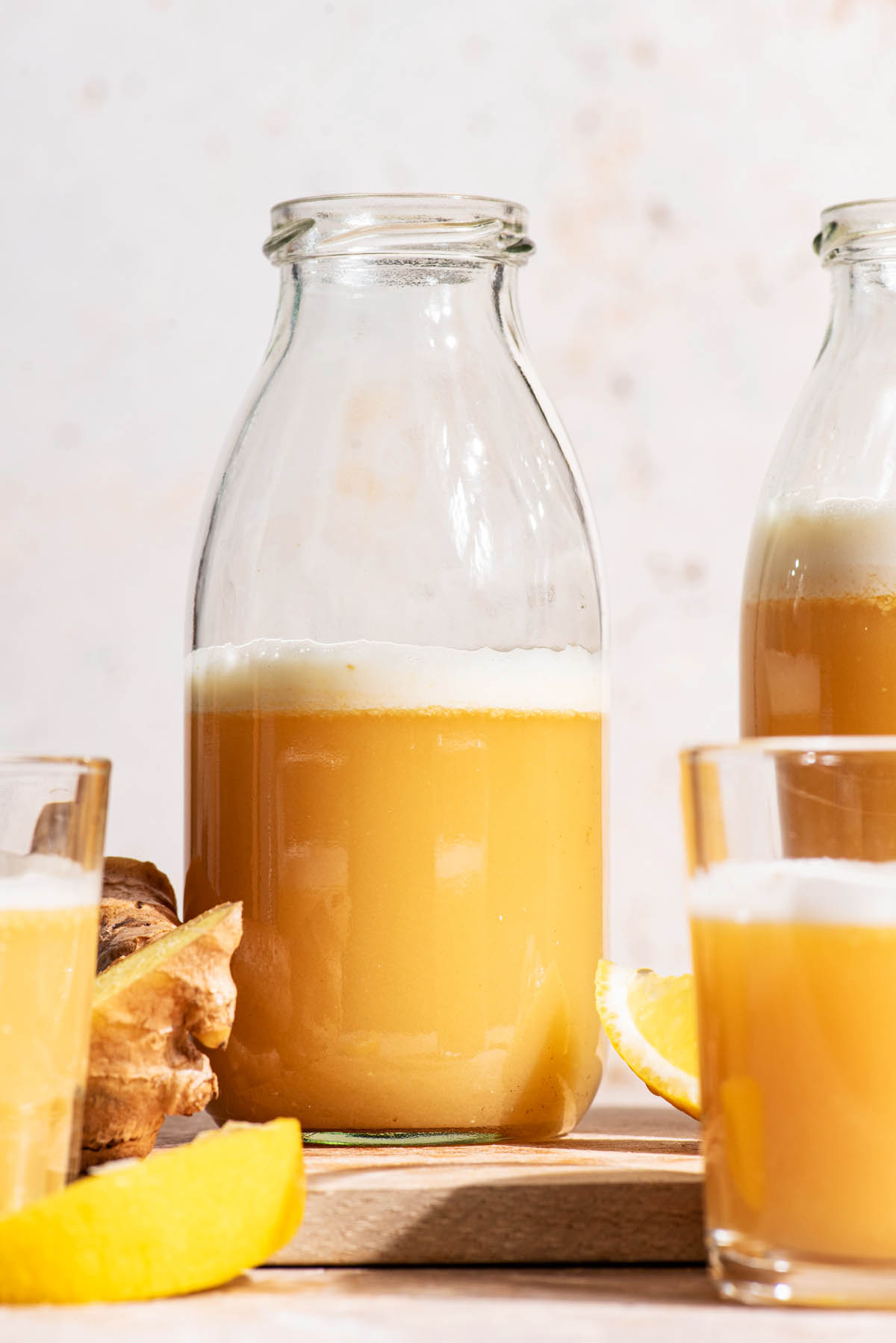 A ginger drink in clear glass bottles and small glasses with lemon and ginger around.