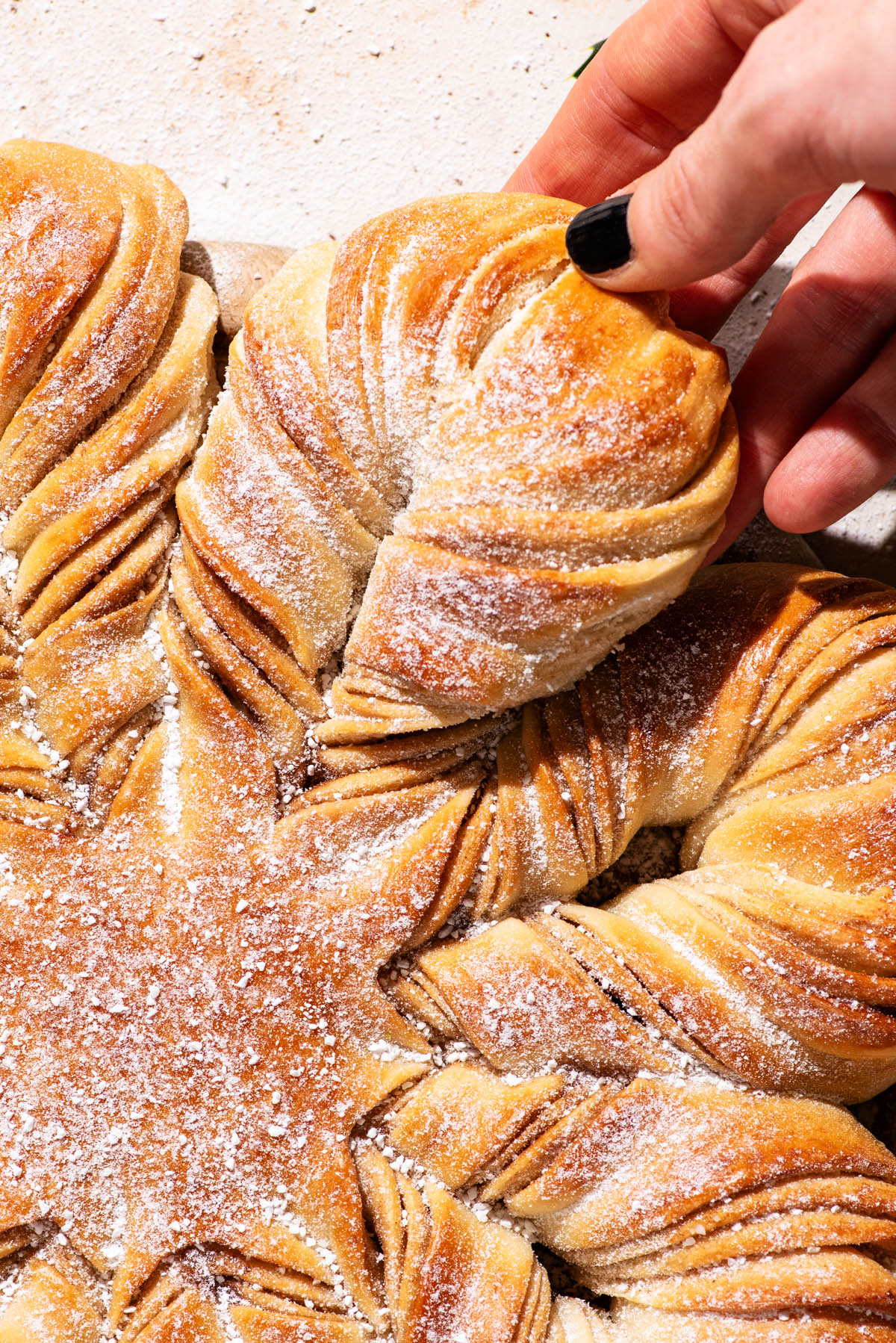 Close up of snowflake bread with a woman's hand lifting a section of the loaf.
