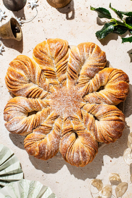 A loaf of star bread on a stone counter with holiday decorations in the corners.