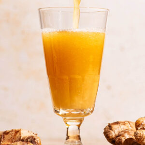A bubbly golden drink being poured into a glass with ginger beside.