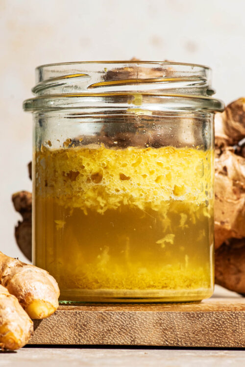 Close up of fermented shredded ginger floating in the water mixture in a glass jar.