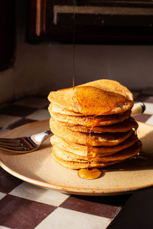A stack of pancakes on a small plate, topped with maple syrup.