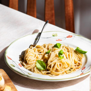 Spaghetti with a light sauce on a plate, topped with basil leaves, at a table setting.