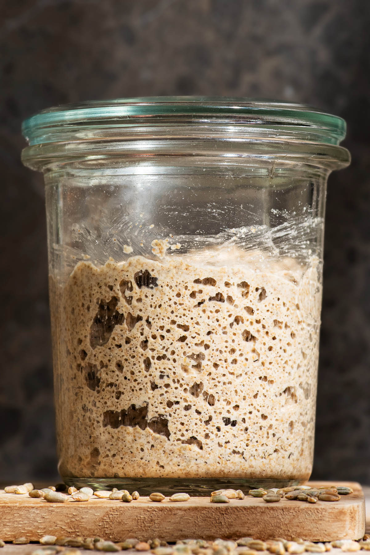 A glass jar with a lid filled with an active whole grain sourdough starter.