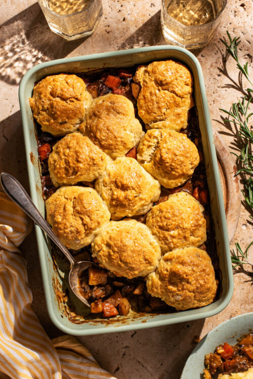 Biscuit-topped vegetable pie in a rectangular baking dish, one scoop removed.