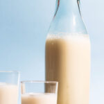 An old glass bottle and two cups filled with a milky drink, whole spelt grains beside.