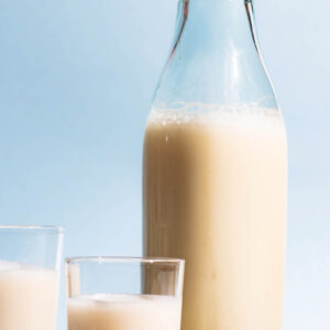 An old glass bottle and two cups filled with a milky drink, whole spelt grains beside.