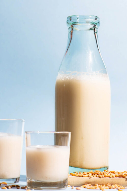 An old glass bottle and two cups filled with a milky drink, whole spelt grains beside.