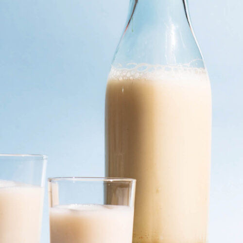 An old glass bottle and two cups filled with a milky drink, whole spelt grains beside.